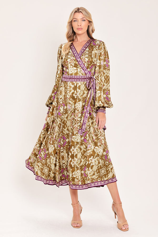 A woman models a long-sleeved midi wrap dress with a brown, beige, and purple floral pattern. The dress features a matching purple patterned belt and hem | Flying Tomato