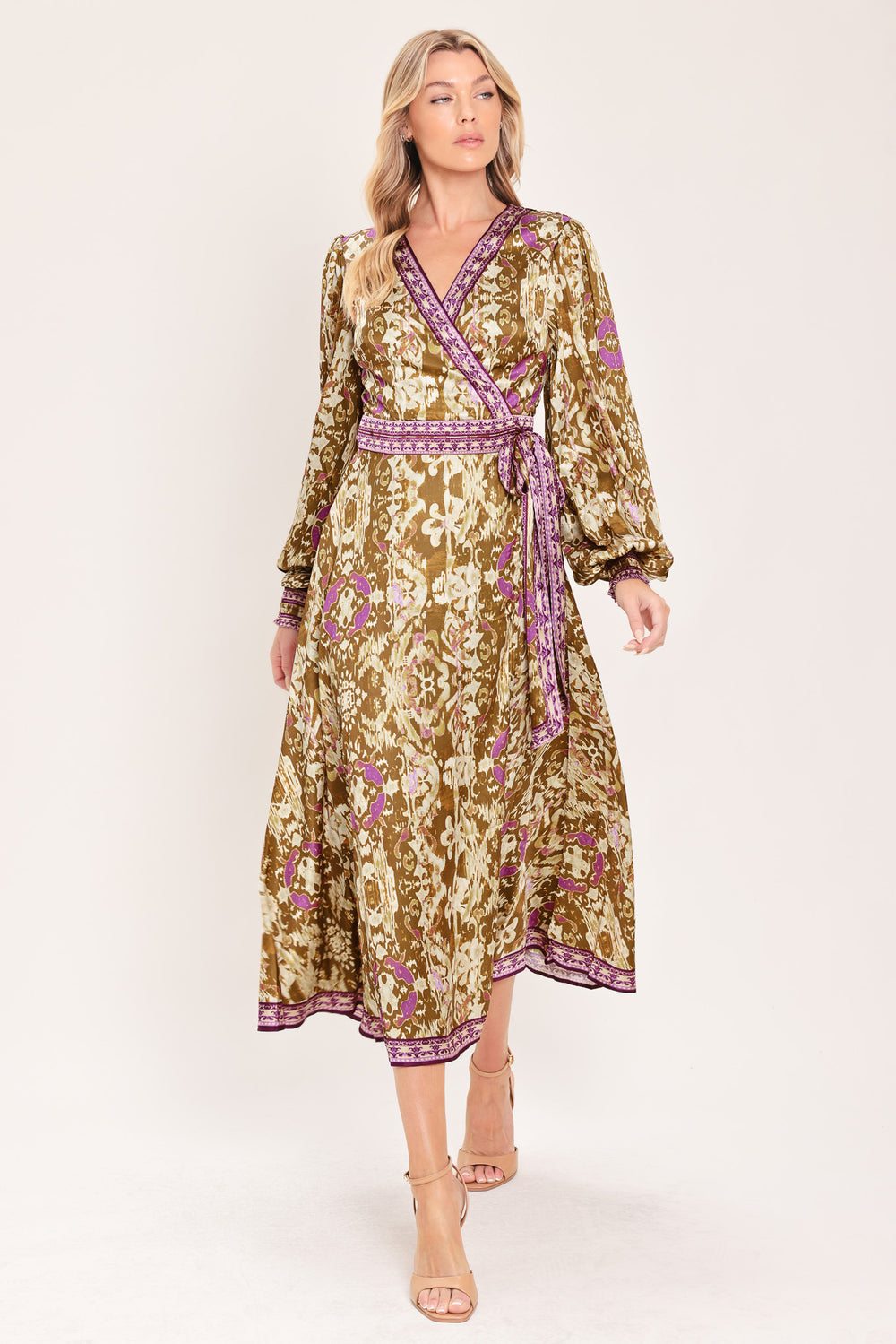 A woman models a long-sleeved midi wrap dress with a brown, beige, and purple floral pattern. The dress features a matching purple patterned belt and hem | Flying Tomato