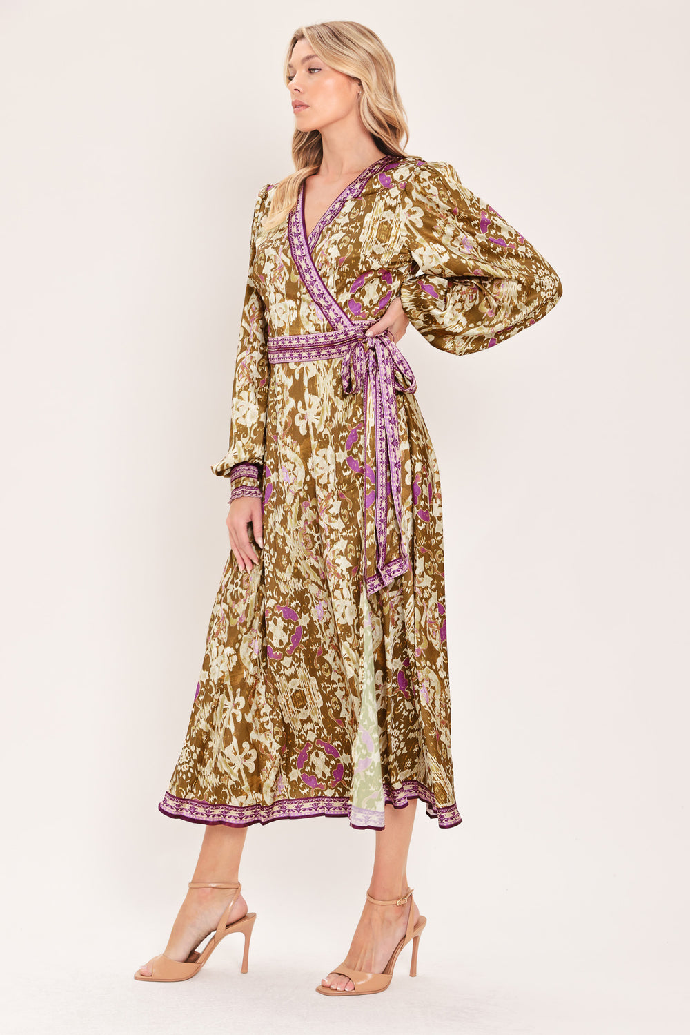 A woman models a long-sleeved midi wrap dress with a brown, beige, and purple floral pattern. The dress features a matching purple patterned belt and hem | Flying Tomato