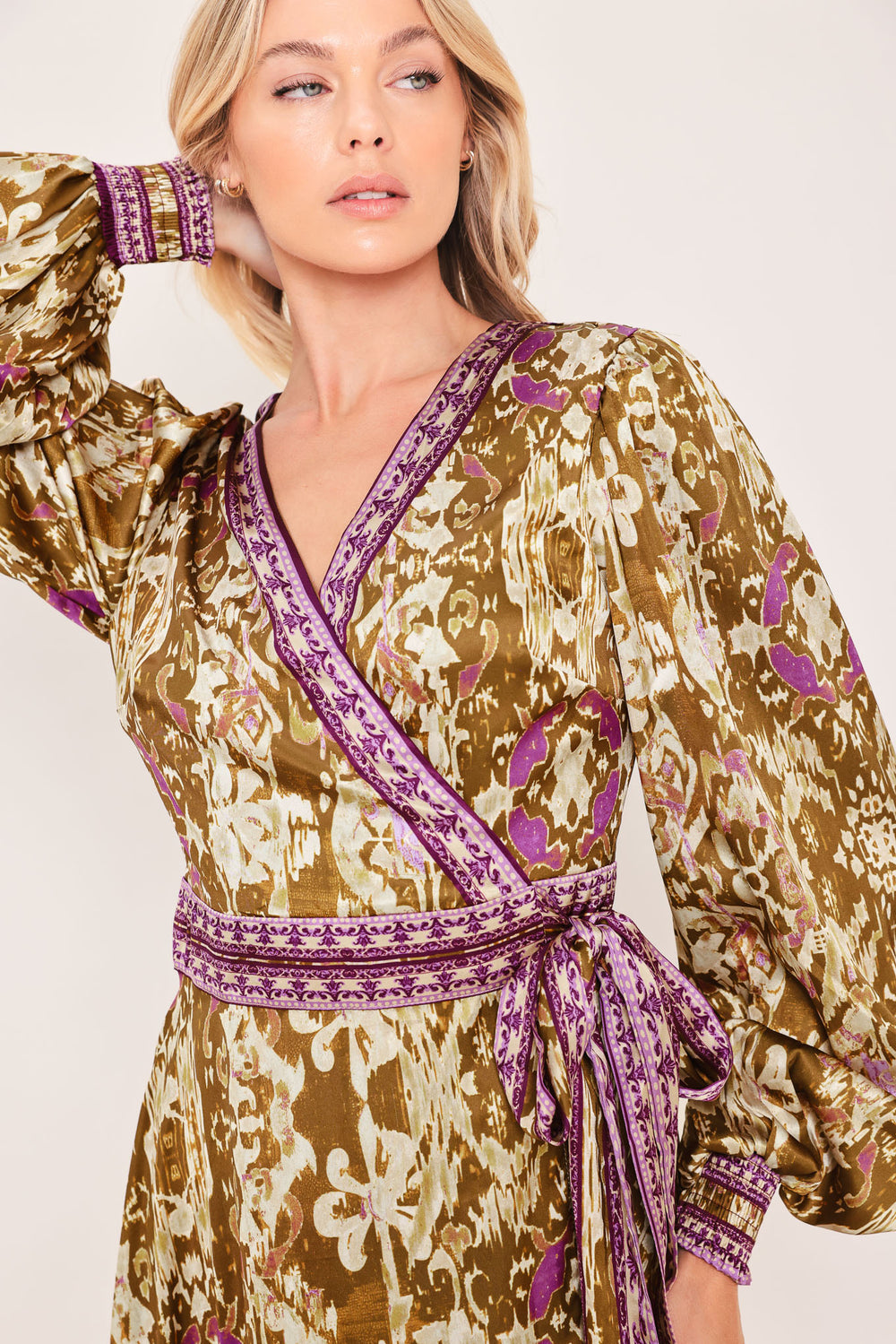 A woman models a long-sleeved midi wrap dress with a brown, beige, and purple floral pattern. The dress features a matching purple patterned belt and hem | Flying Tomato