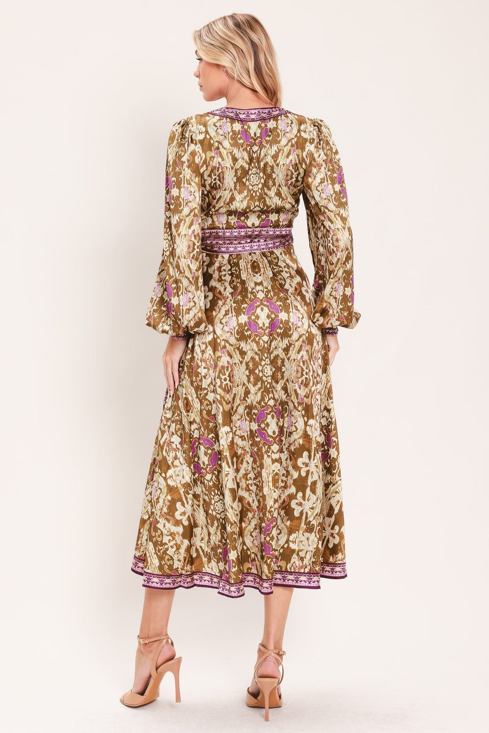 A woman models a long-sleeved midi wrap dress with a brown, beige, and purple floral pattern. The dress features a matching purple patterned belt and hem | Flying Tomato