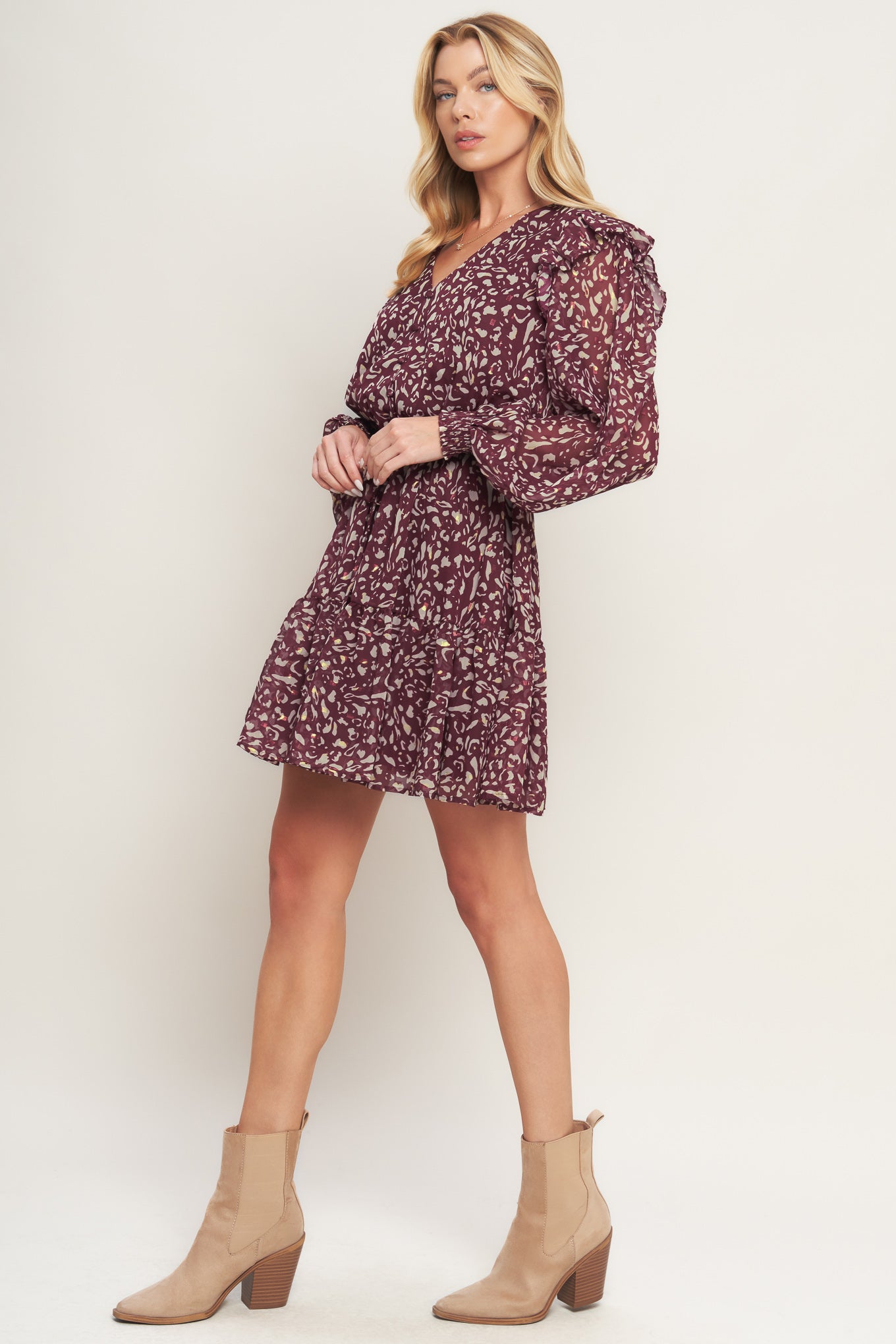 A printed woven mini dress featuring V neckline, long sleeve with ruffled shoulder, front button detail, elasticized waist with front tie and ruffled hemline