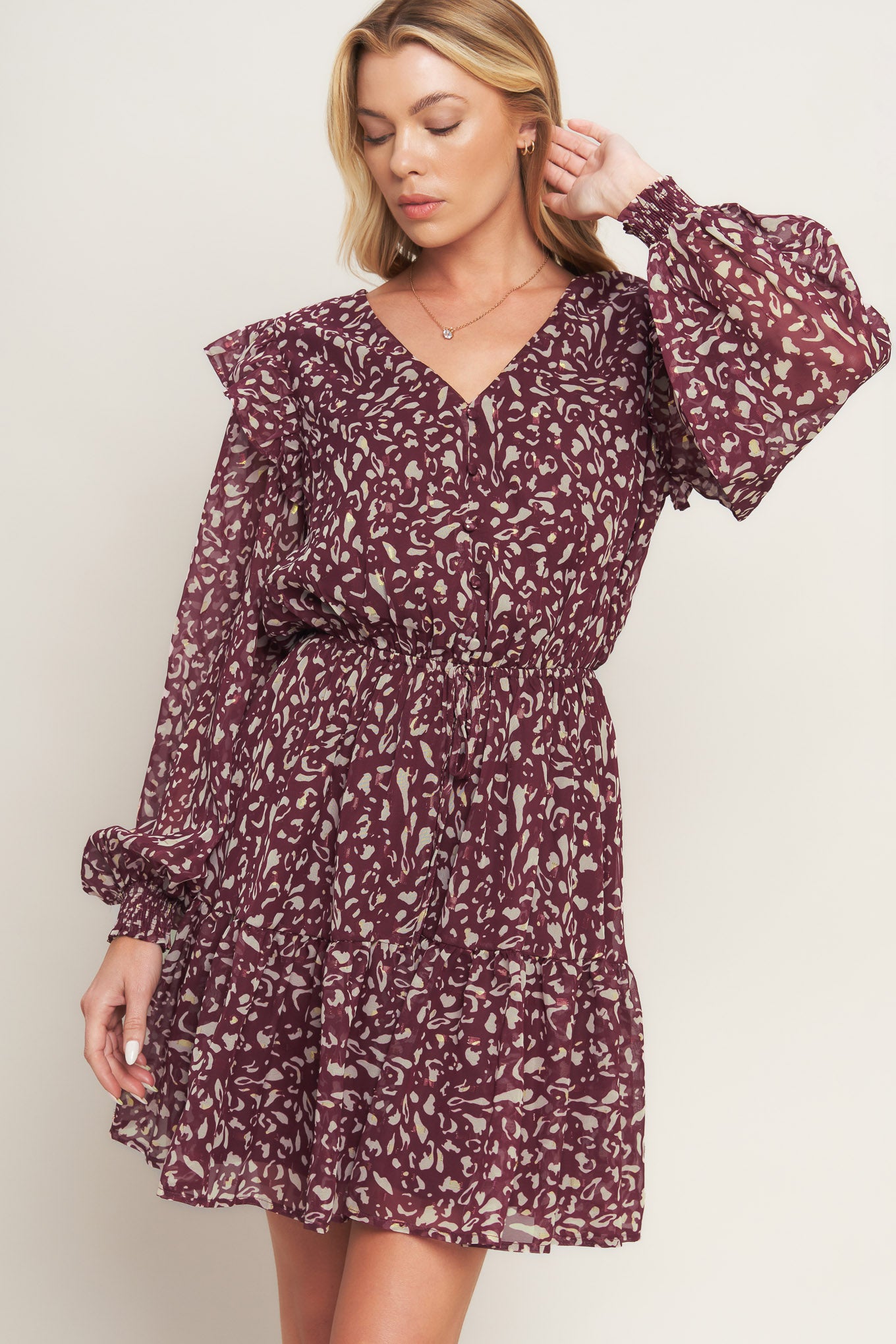 A printed woven mini dress featuring V neckline, long sleeve with ruffled shoulder, front button detail, elasticized waist with front tie and ruffled hemline