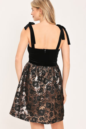 Woman wearing a sleeveless mini dress with a black velvet square neck top with lace up shoulder straps and bronze circle skirt with black jacquard flowers | Flying Tomato