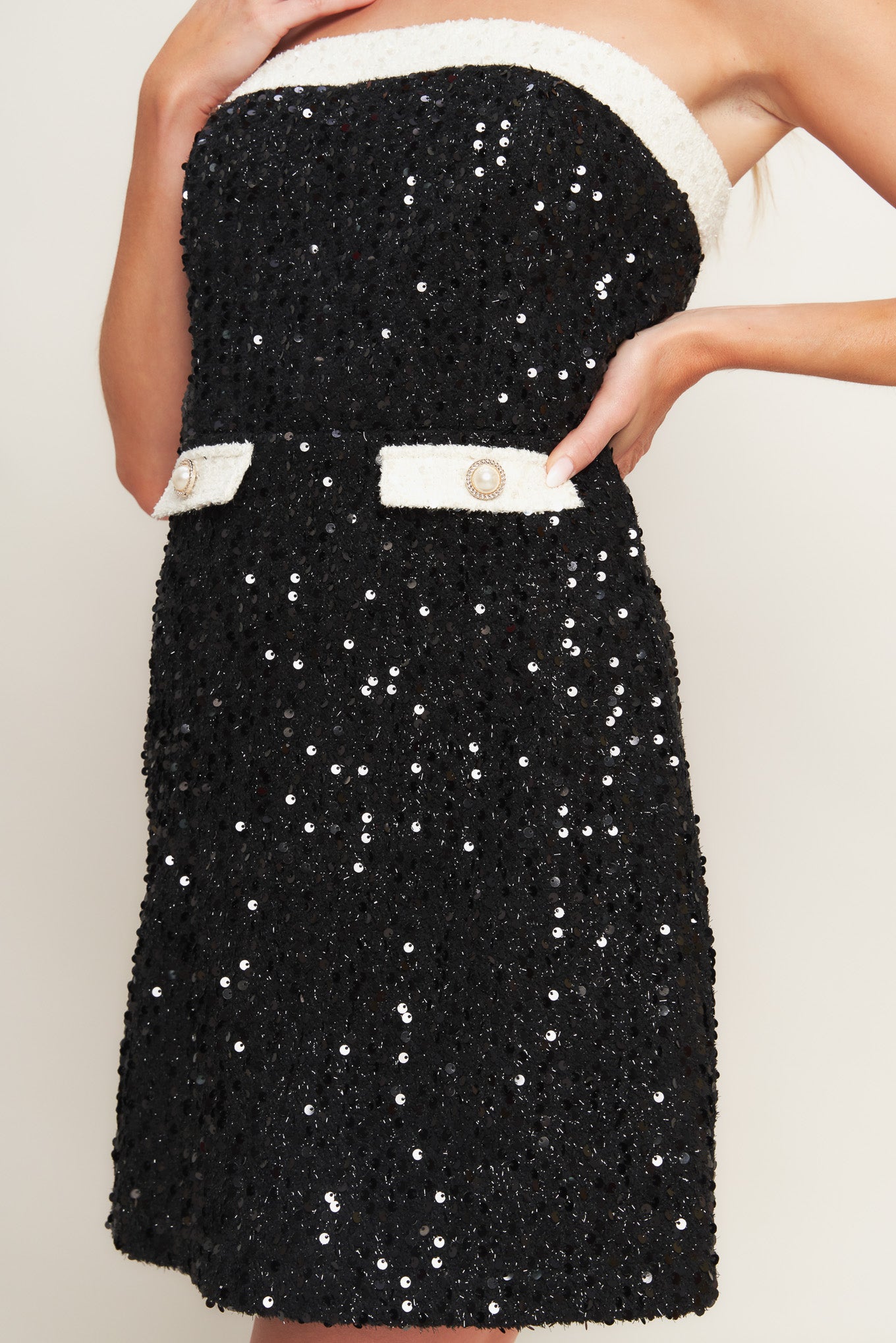 A sequin mini dress featuring strapless neckline, front pocket flap with button and back zipper closure