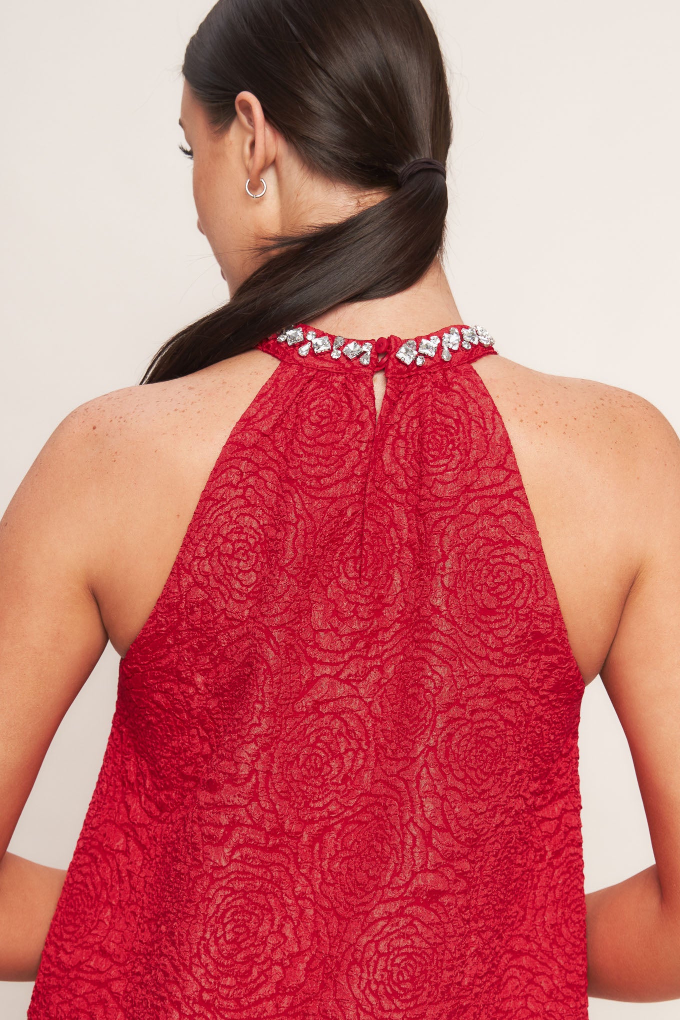 A textured woven mini dress featuring halter neckline with jewel embellishment, double ruffled hem and back neck button closure