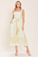 Woman wearing a ivory sleeveless dress with gold embroidery featuring straight neckline, straps, self sash tie with tassel, full skirt and smocked back bodice | Flying Tomato