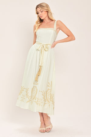 Woman wearing a ivory sleeveless dress with gold embroidery featuring straight neckline, straps, self sash tie with tassel, full skirt and smocked back bodice | Flying Tomato