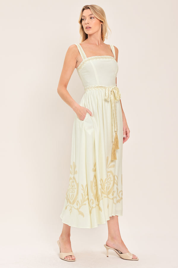 Woman wearing a ivory sleeveless dress with gold embroidery featuring straight neckline, straps, self sash tie with tassel, full skirt and smocked back bodice | Flying Tomato