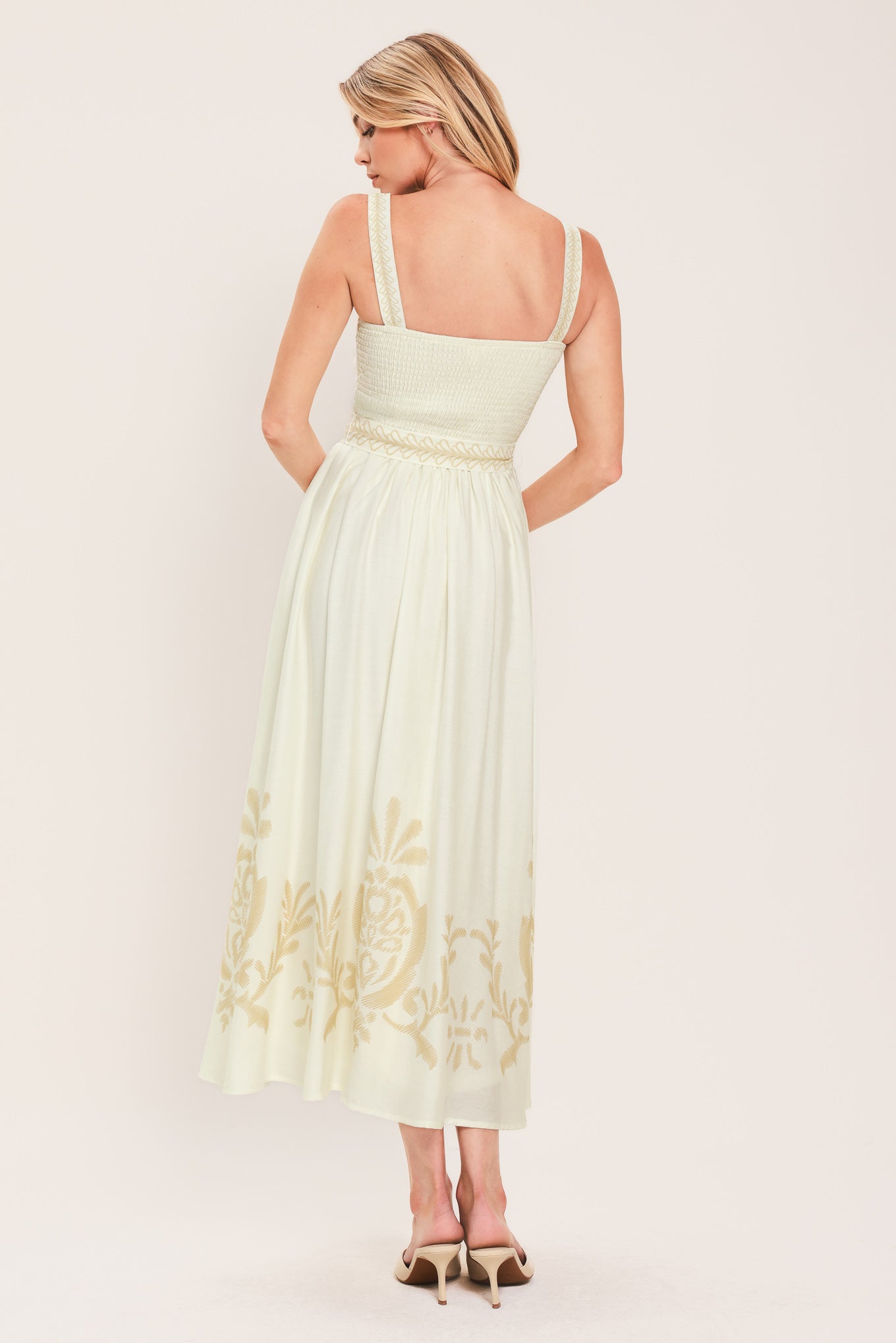 Woman wearing a ivory sleeveless dress with gold embroidery featuring straight neckline, straps, self sash tie with tassel, full skirt and smocked back bodice | Flying Tomato