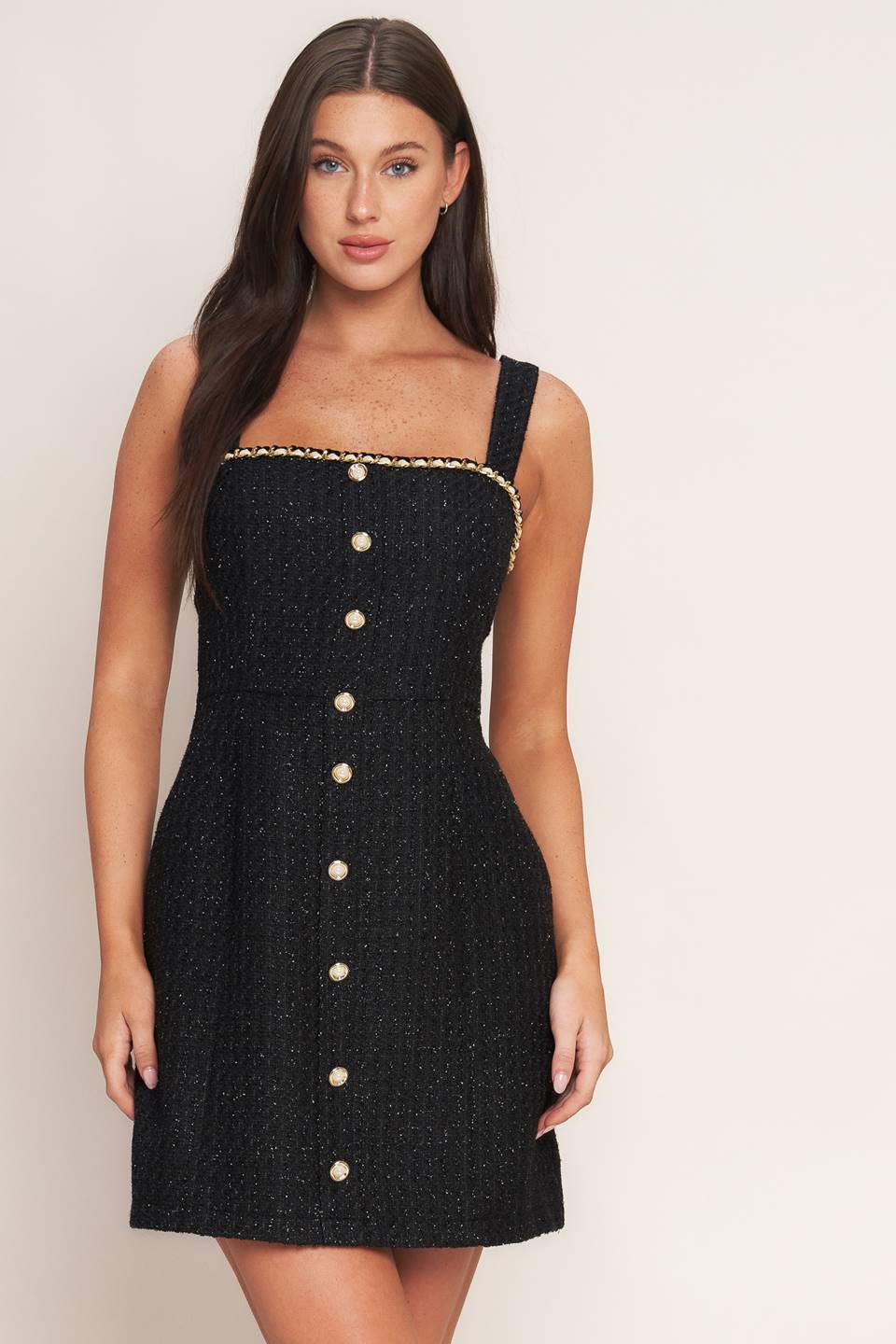 A tweed mini dress featuring trimmed straight neckline, straps, front button down detail and back zipper closure