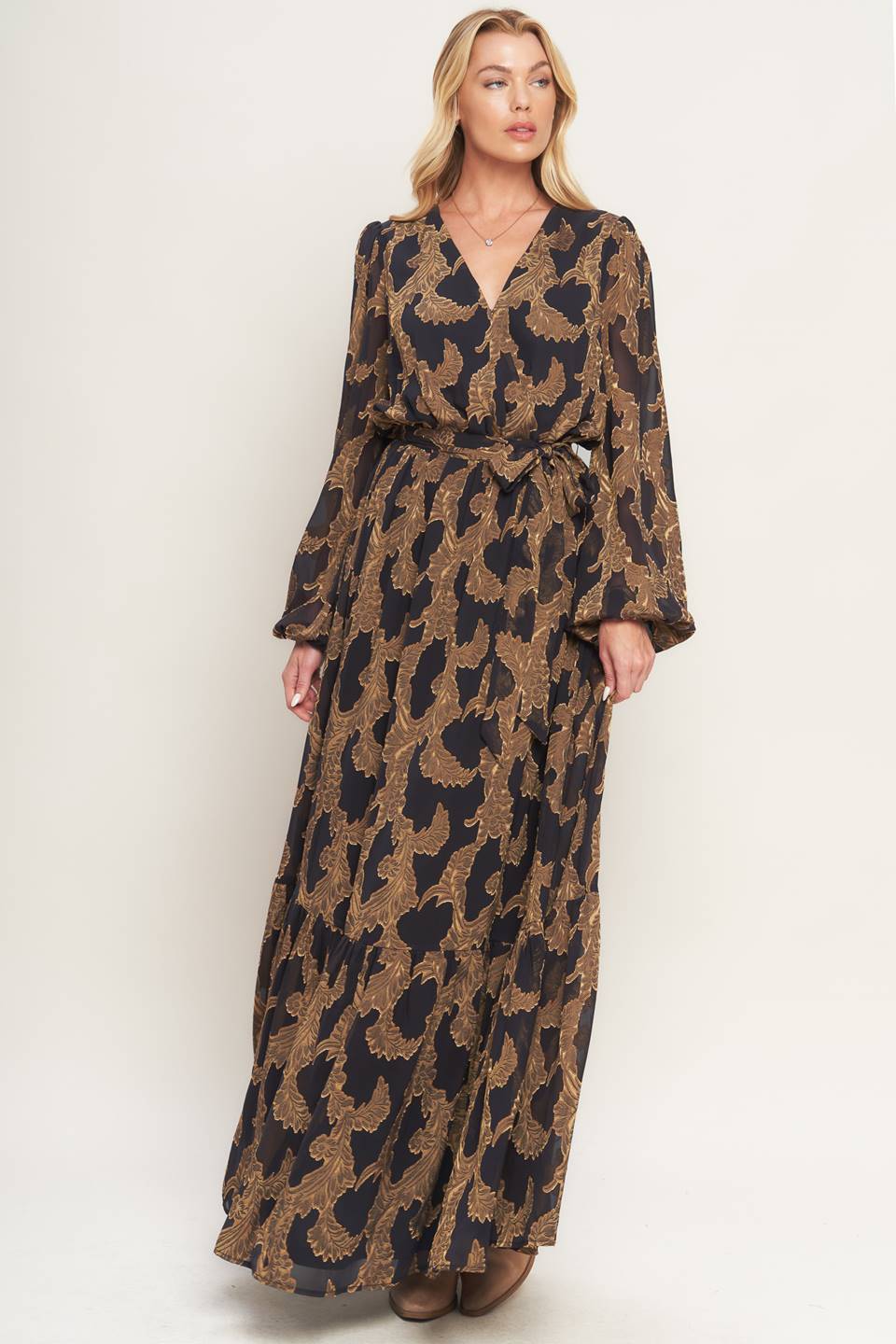 A woven jacquard maxi dress featuring surplice neckline, long sleeve, elasticized waist with self sash and ruffled hemline