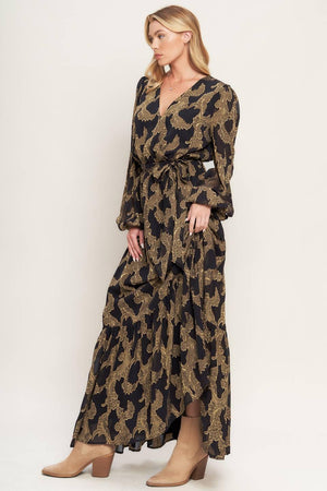 A woven jacquard maxi dress featuring surplice neckline, long sleeve, elasticized waist with self sash and ruffled hemline
