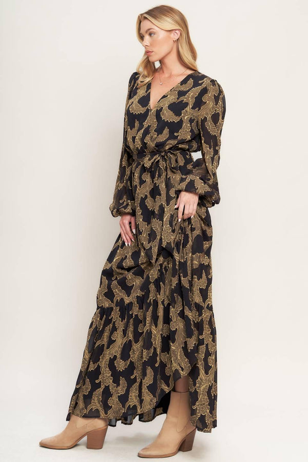 A woven jacquard maxi dress featuring surplice neckline, long sleeve, elasticized waist with self sash and ruffled hemline