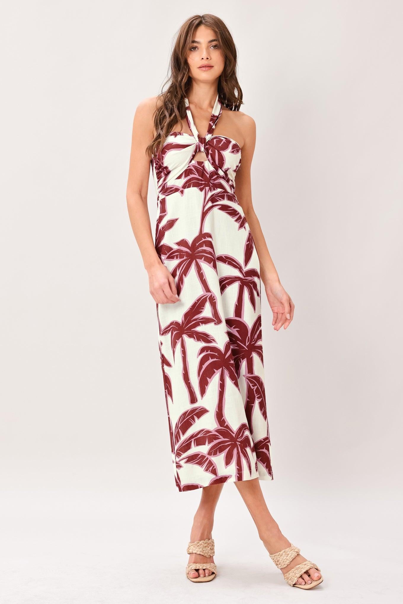 Woman wearing a white with red palm tree pattern printed woven midi dress featuring halter neckline, shirred bodice with center loop and cut out, straight skirt, bare back and zipper closure