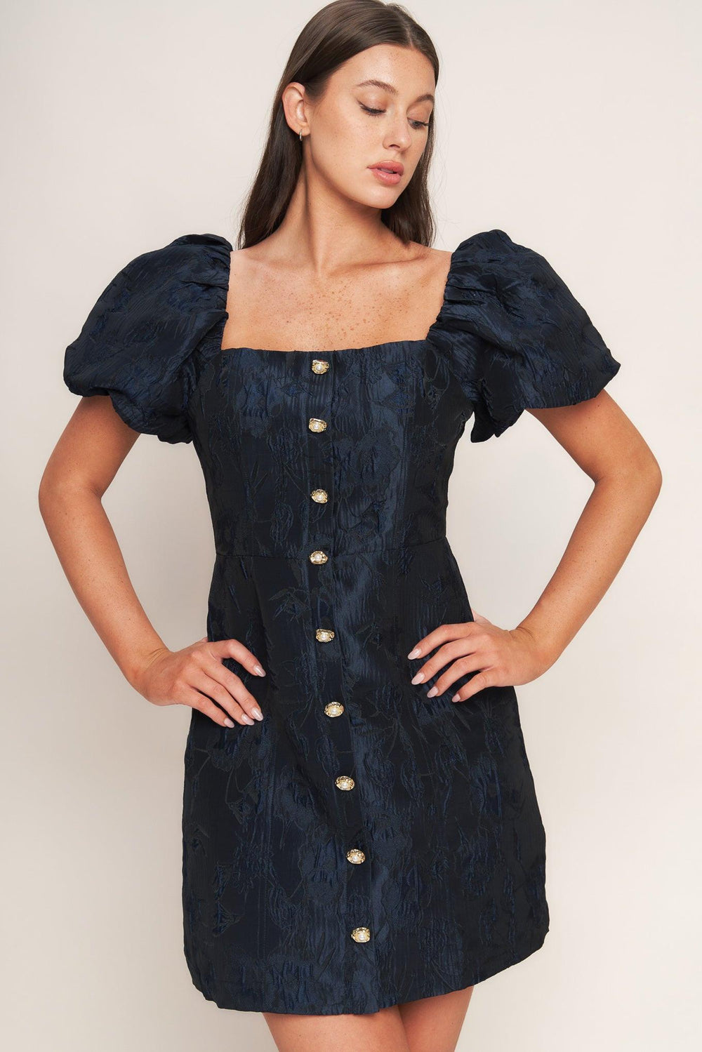 A textured woven mini dress featuring square neckline, short puff sleeve, front button down detail and back zipper closure