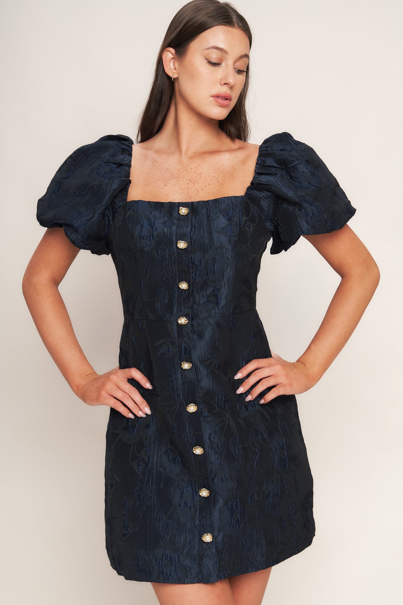 A textured woven mini dress featuring square neckline, short puff sleeve, front button down detail and back zipper closure