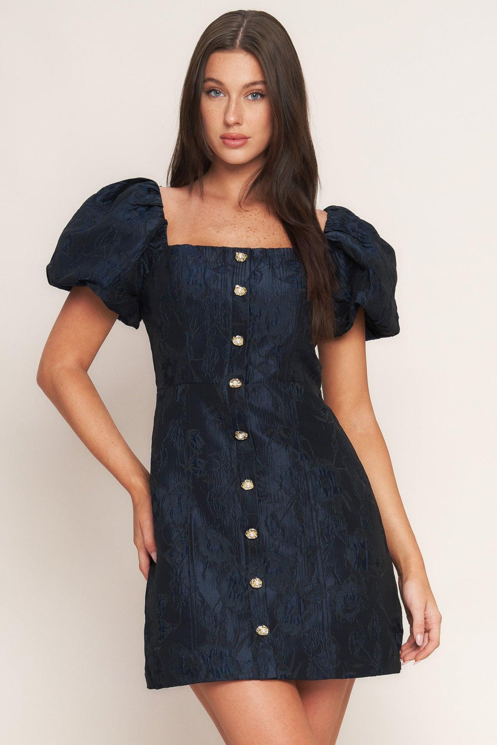 A textured woven mini dress featuring square neckline, short puff sleeve, front button down detail and back zipper closure