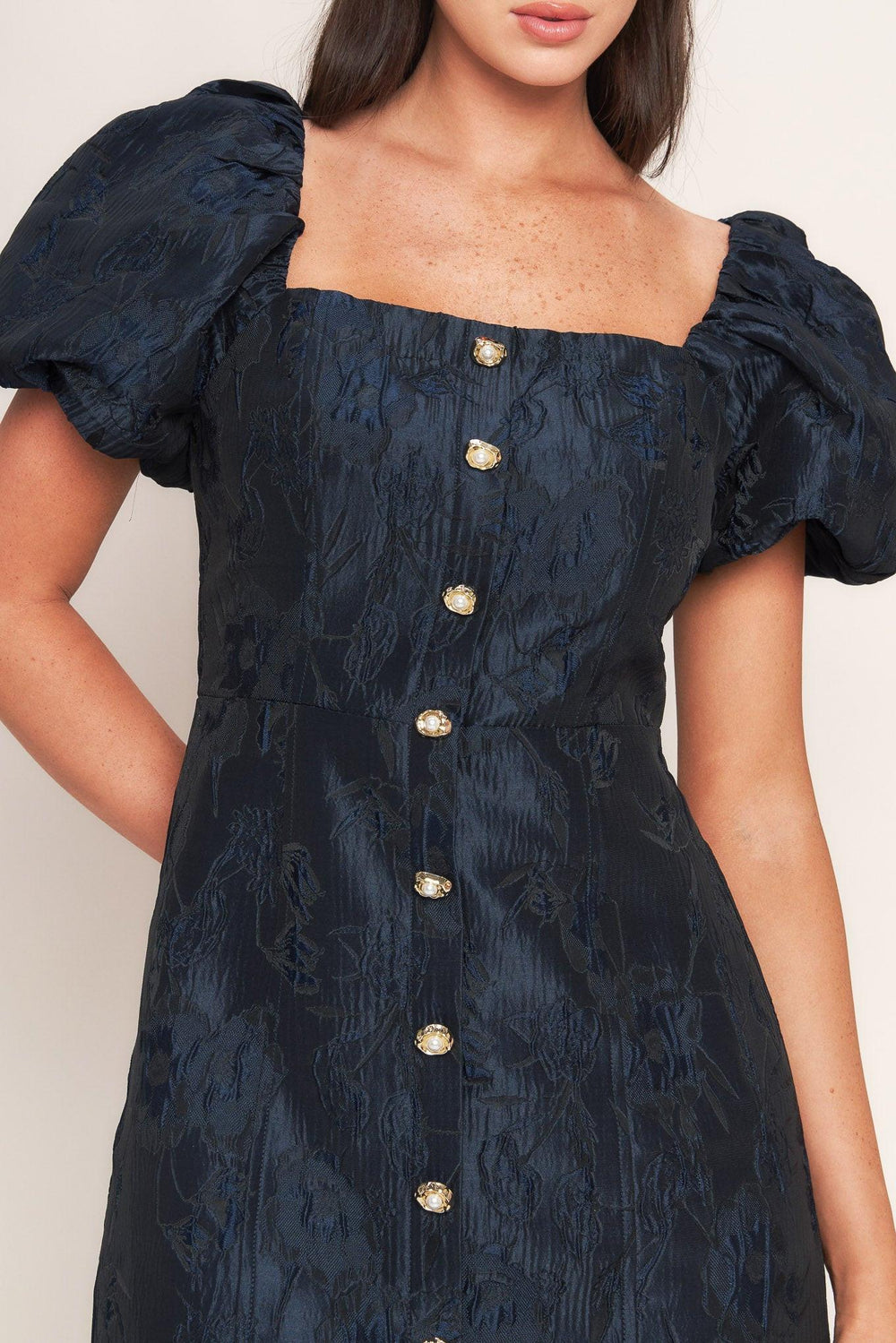 A textured woven mini dress featuring square neckline, short puff sleeve, front button down detail and back zipper closure