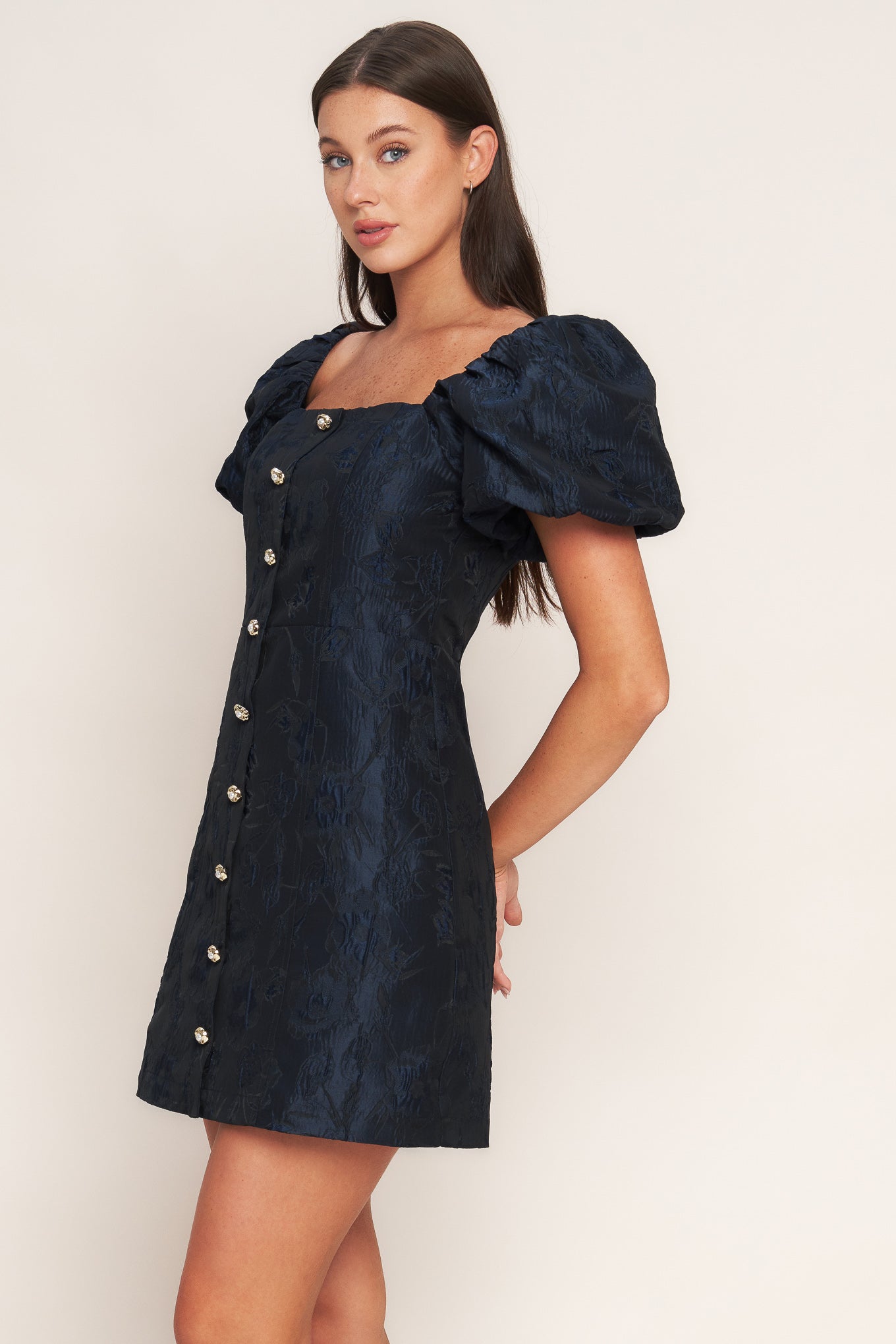 A textured woven mini dress featuring square neckline, short puff sleeve, front button down detail and back zipper closure
