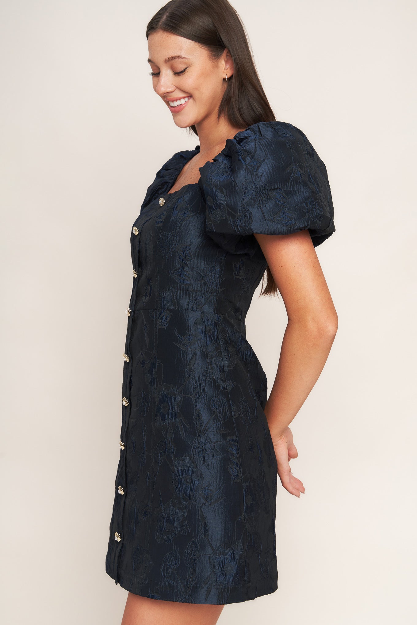 A textured woven mini dress featuring square neckline, short puff sleeve, front button down detail and back zipper closure
