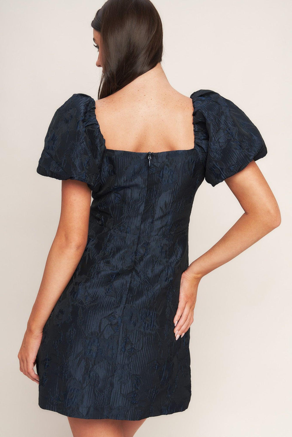 A textured woven mini dress featuring square neckline, short puff sleeve, front button down detail and back zipper closure