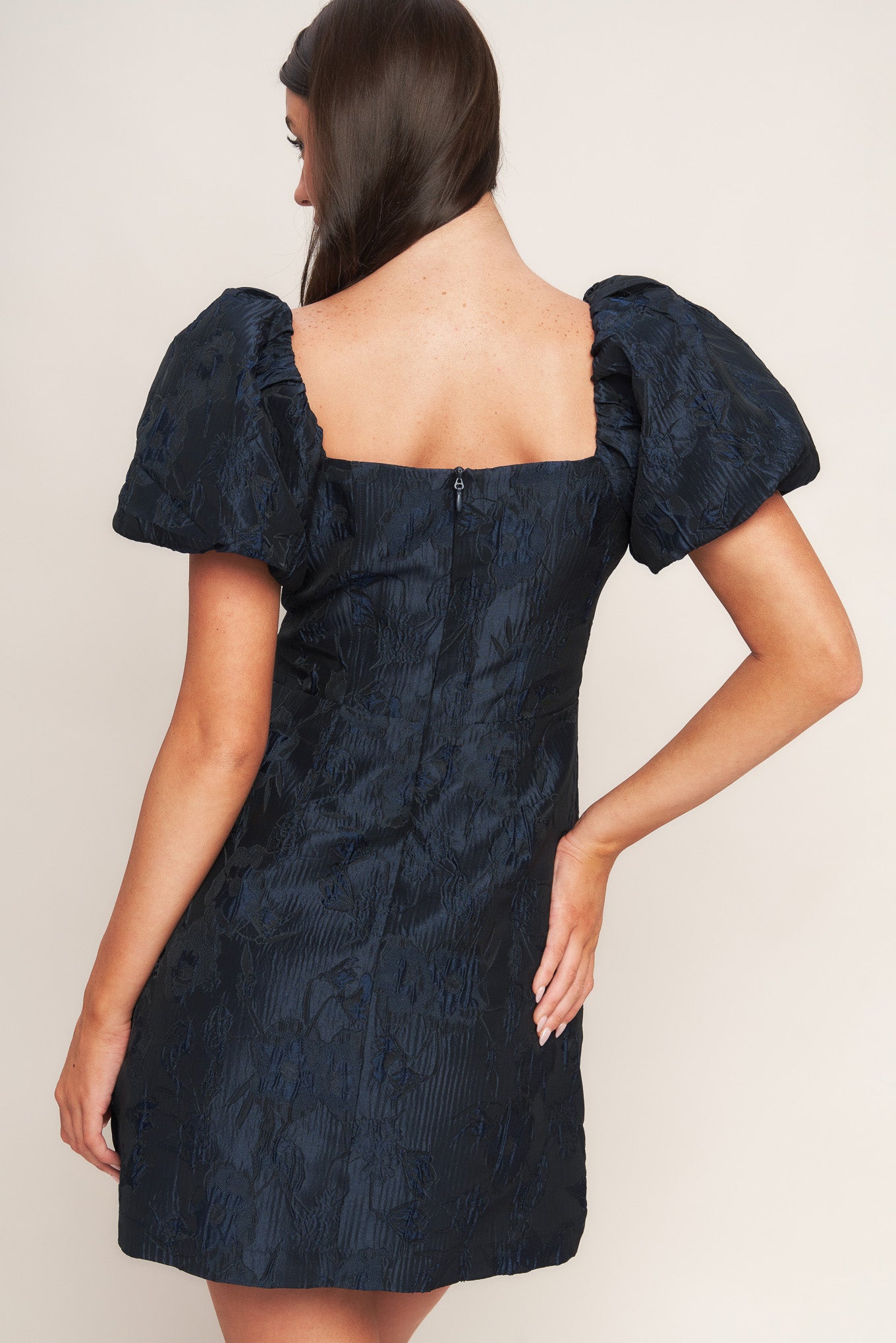 A textured woven mini dress featuring square neckline, short puff sleeve, front button down detail and back zipper closure