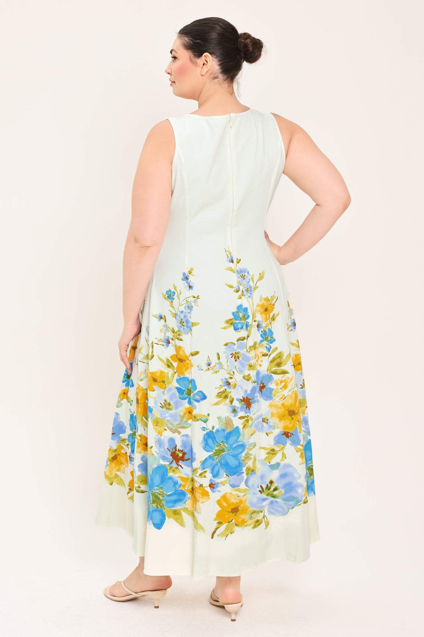 A woman modeling a sleeveless midi dress with a square neckline and a white base featuring a blue and yellow floral print on the skirt | Plus Curve Flying Tomato