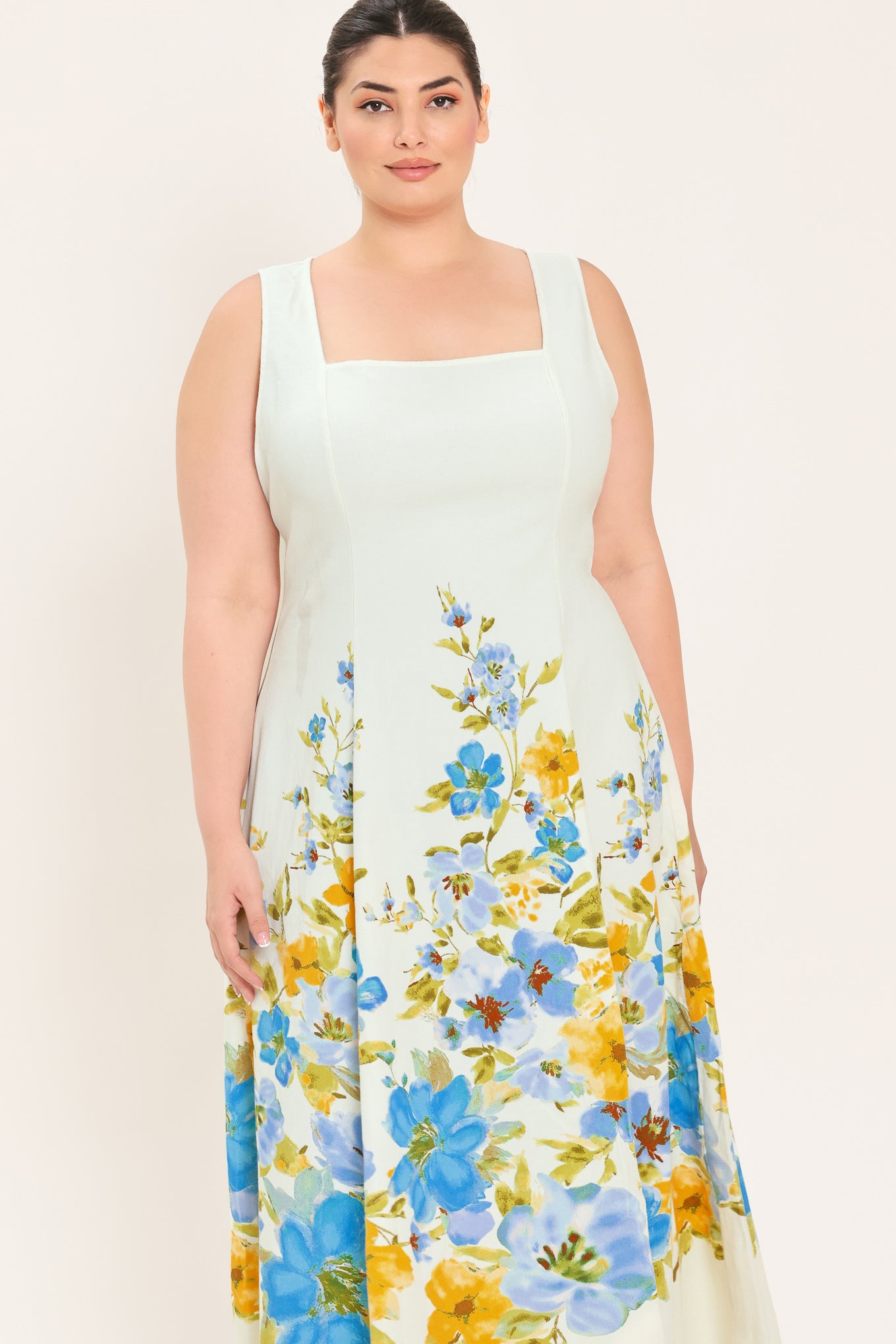 A woman modeling a sleeveless midi dress with a square neckline and a white base featuring a blue and yellow floral print on the skirt | Plus Curve Flying Tomato