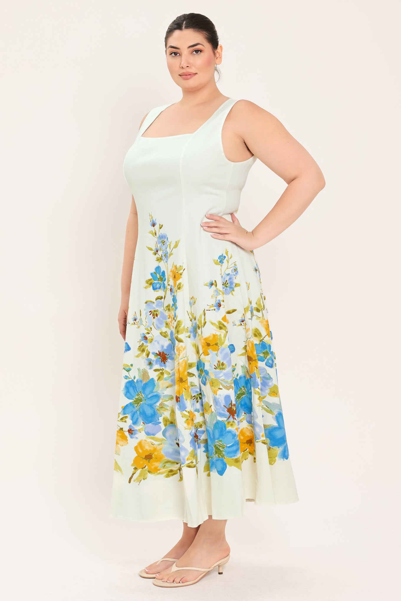 A woman modeling a sleeveless midi dress with a square neckline and a white base featuring a blue and yellow floral print on the skirt | Plus Curve Flying Tomato