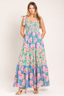Woman wearing a floral maxi dress featuring straight neckline with ruffle edge, shoulder tie, smocked bodice and tier skirt | Flying Tomato