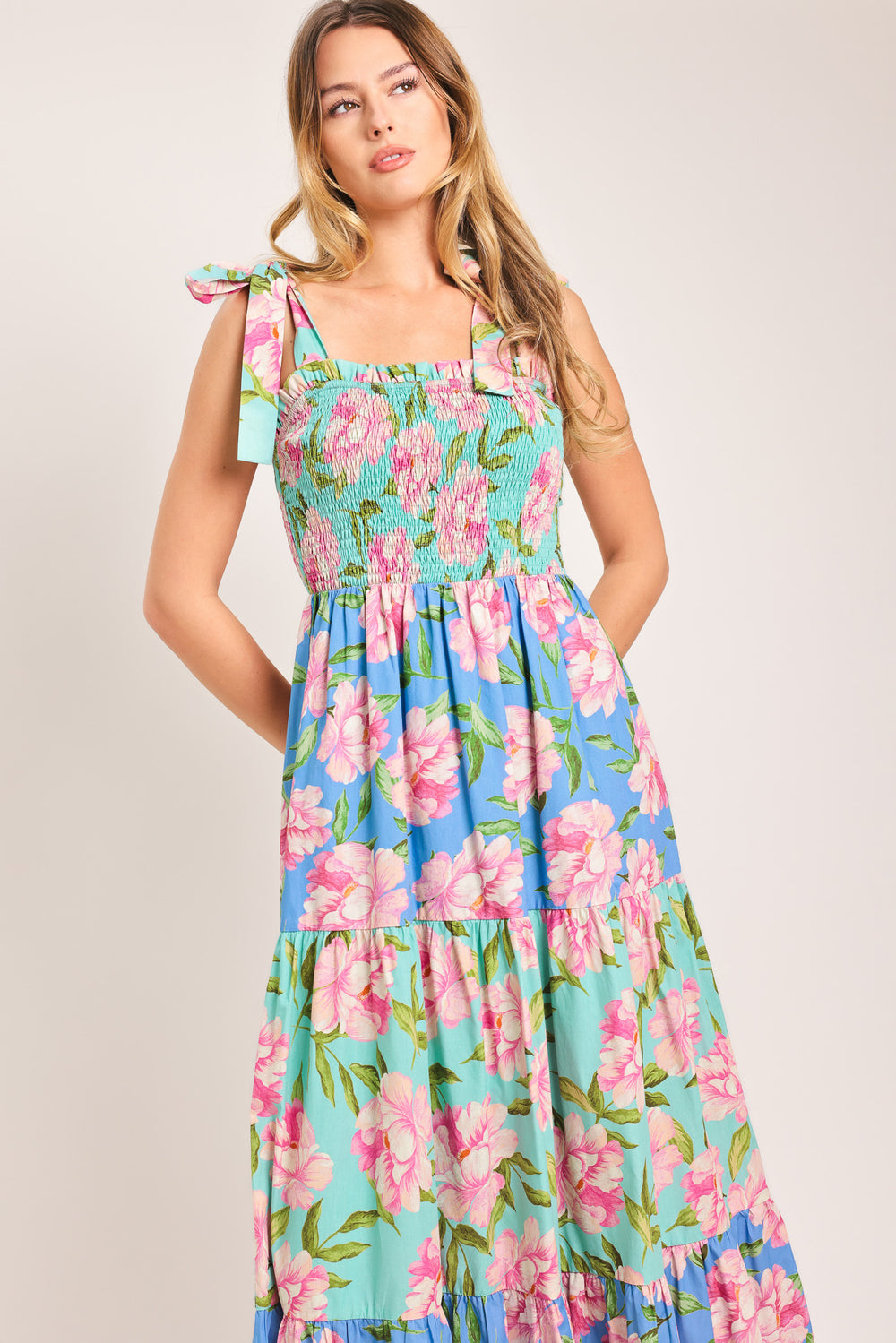 Woman wearing a floral maxi dress featuring straight neckline with ruffle edge, shoulder tie, smocked bodice and tier skirt | Flying Tomato
