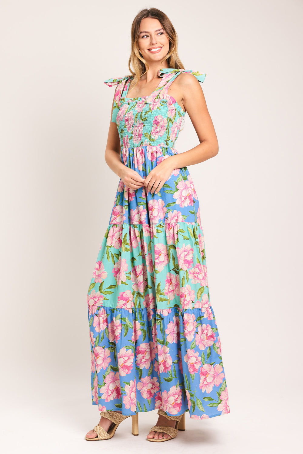Woman wearing a floral maxi dress featuring straight neckline with ruffle edge, shoulder tie, smocked bodice and tier skirt | Flying Tomato