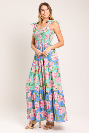 Woman wearing a floral maxi dress featuring straight neckline with ruffle edge, shoulder tie, smocked bodice and tier skirt | Flying Tomato