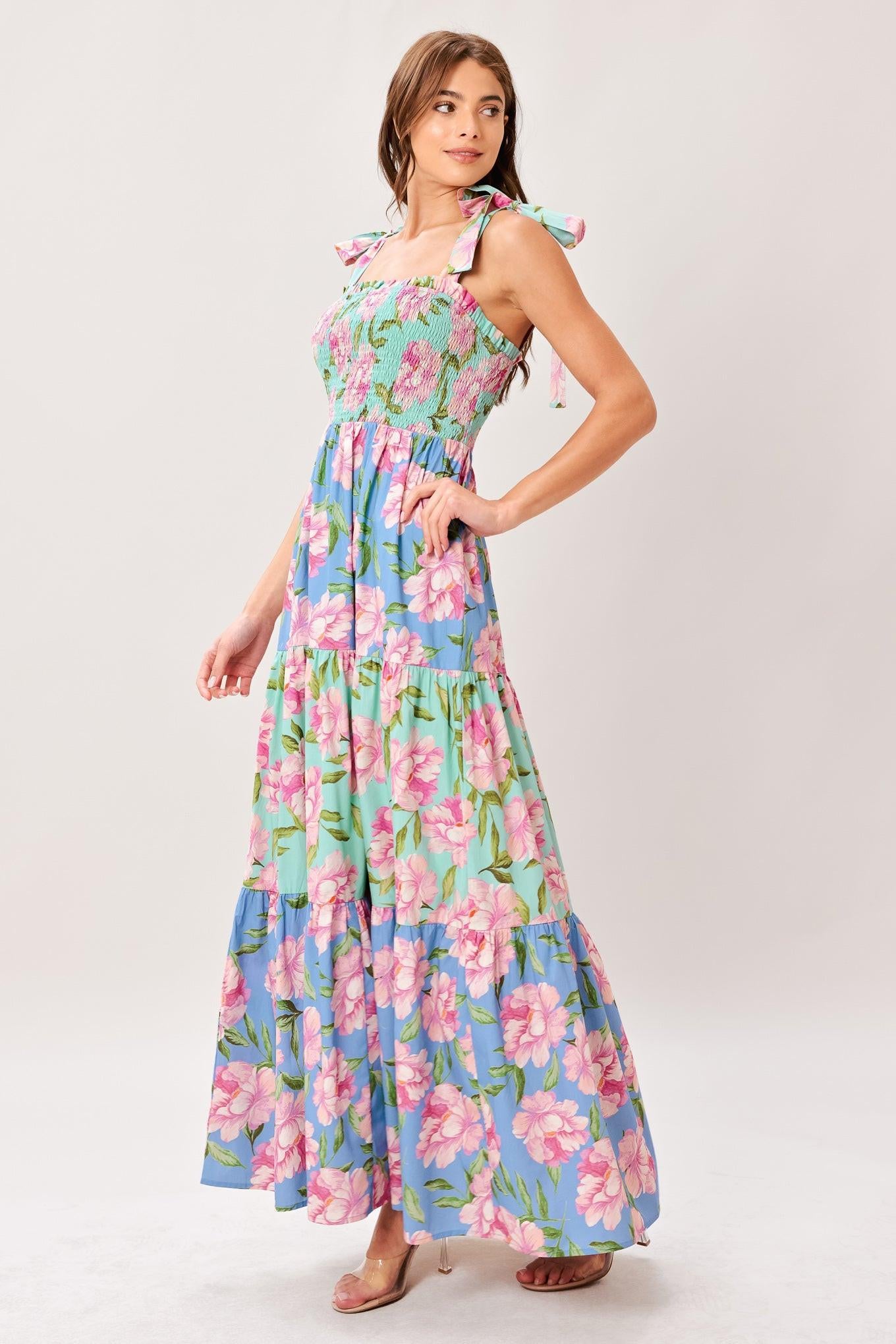 Woman wearing a floral printed woven maxi dress featuring straight neckline with ruffle edge, shoulder tie, smocked bodice and tier skirt