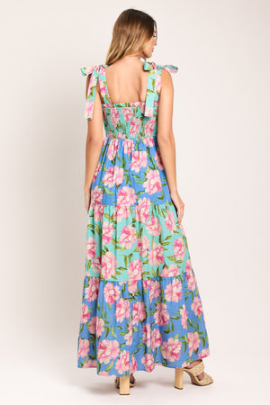 Woman wearing a floral maxi dress featuring straight neckline with ruffle edge, shoulder tie, smocked bodice and tier skirt | Flying Tomato