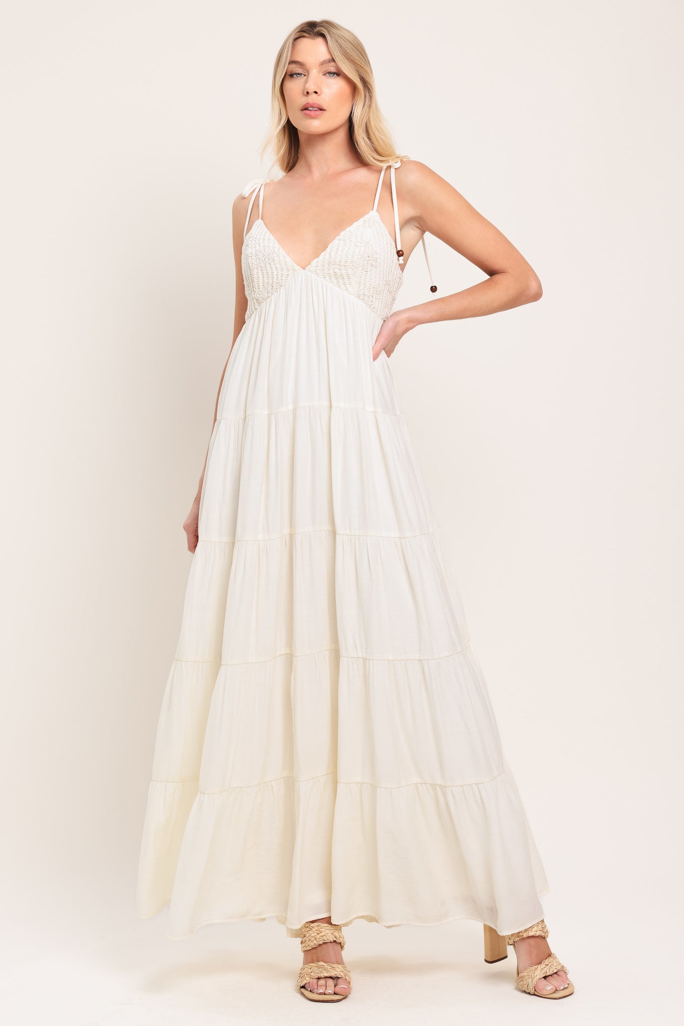 Woman wearing a cream flowy maxi dress featuring lace bodice, shoulder tie, tier body and smocked back bodice | Flying Tomato