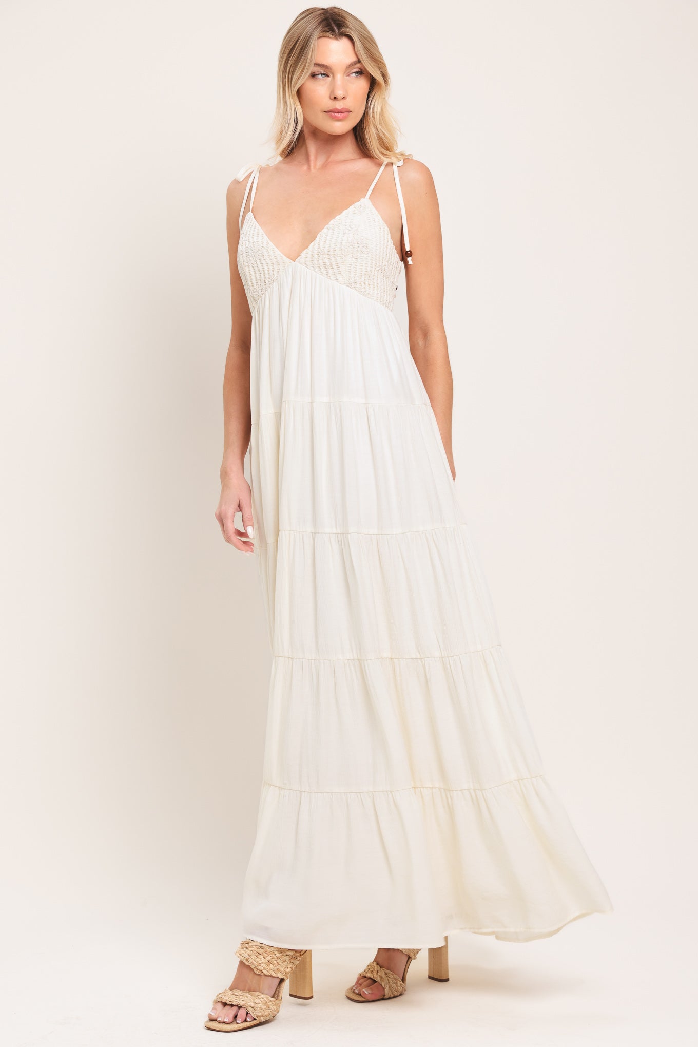 Woman wearing a cream flowy maxi dress featuring lace bodice, shoulder tie, tier body and smocked back bodice | Flying Tomato