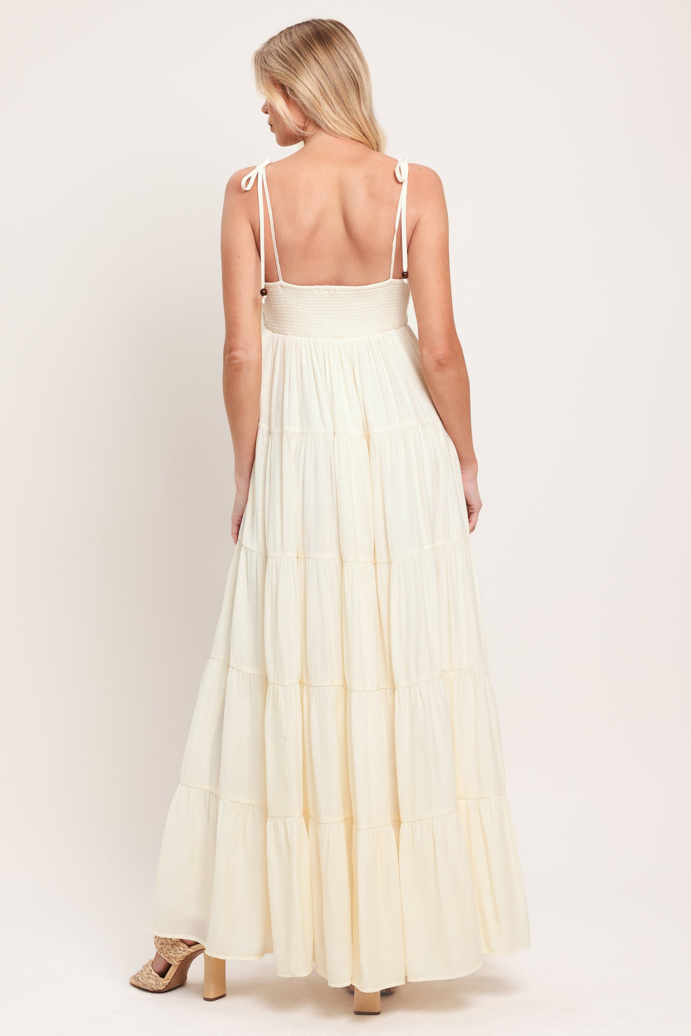 Woman wearing a cream flowy maxi dress featuring lace bodice, shoulder tie, tier body and smocked back bodice | Flying Tomato