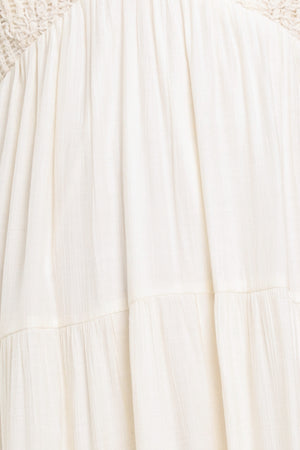 Woman wearing a cream flowy maxi dress featuring lace bodice, shoulder tie, tier body and smocked back bodice | Flying Tomato