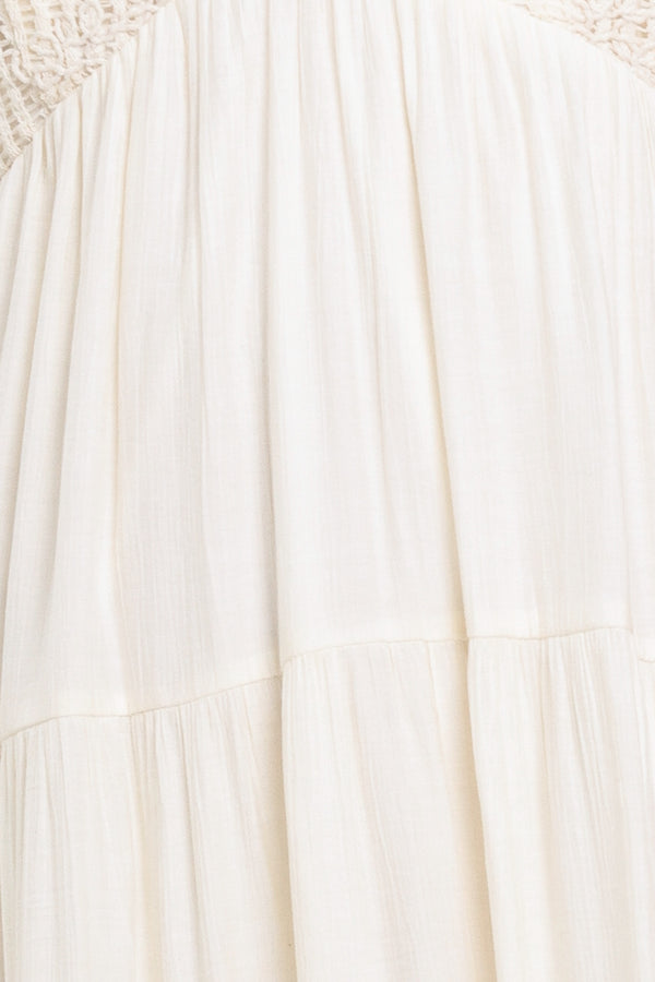 Woman wearing a cream flowy maxi dress featuring lace bodice, shoulder tie, tier body and smocked back bodice | Flying Tomato