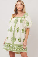 Woman wearing a white printed woven mini dress with green embroidery featuring a square neckline, short puff sleeve and front button detail on a white background | Flying Tomato