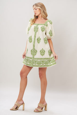 Woman wearing a white printed woven mini dress with green embroidery featuring a square neckline, short puff sleeve and front button detail on a white background | Flying Tomato