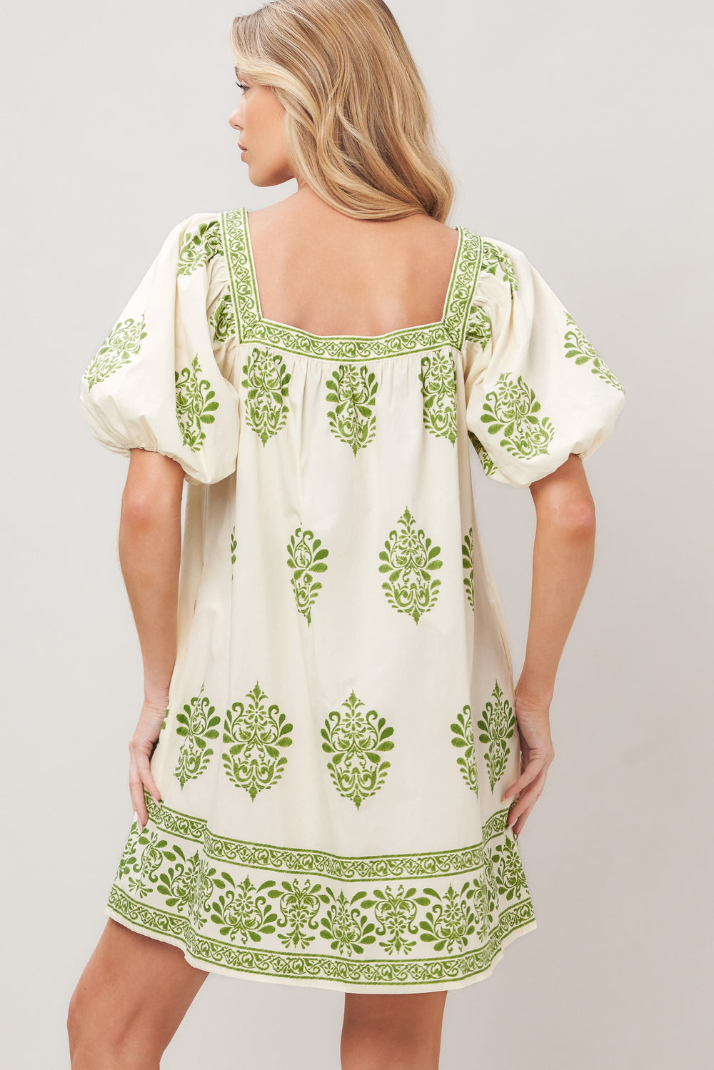 Woman wearing a white printed woven mini dress with green embroidery featuring a square neckline, short puff sleeve and front button detail on a white background | Flying Tomato