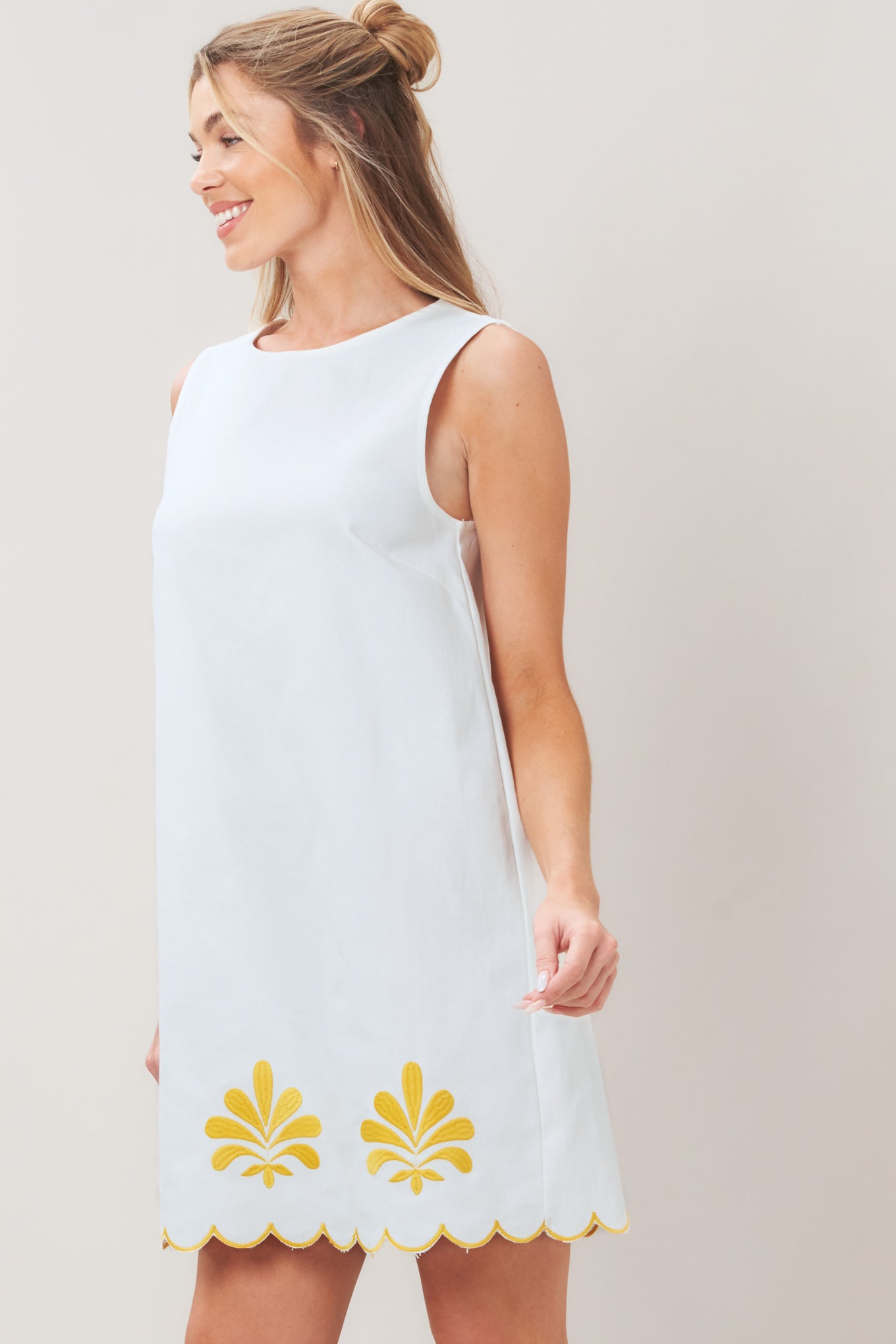 Woman wearing a white dress with yellow floral patterns on a plain background | Flying Tomato