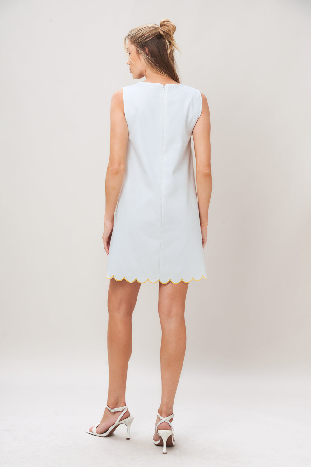 Woman wearing a white dress with yellow floral patterns on a plain background | Flying Tomato