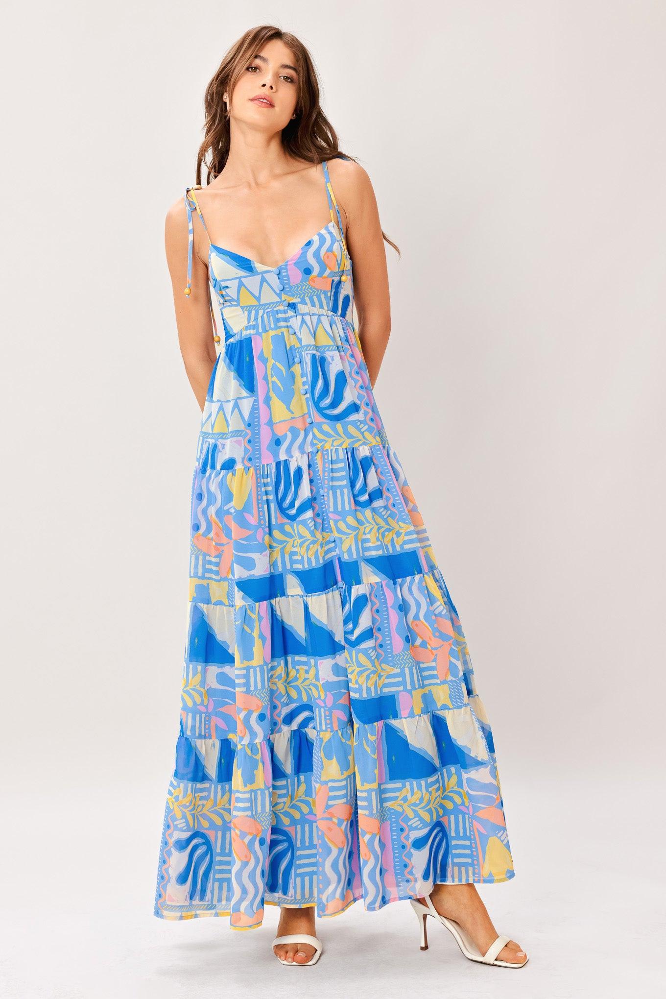 Woman wearing a colorful geometric patterned printed woven maxi dress featuring cami top with shoulder tie, front button detail, tier skirt and smocked back bodice