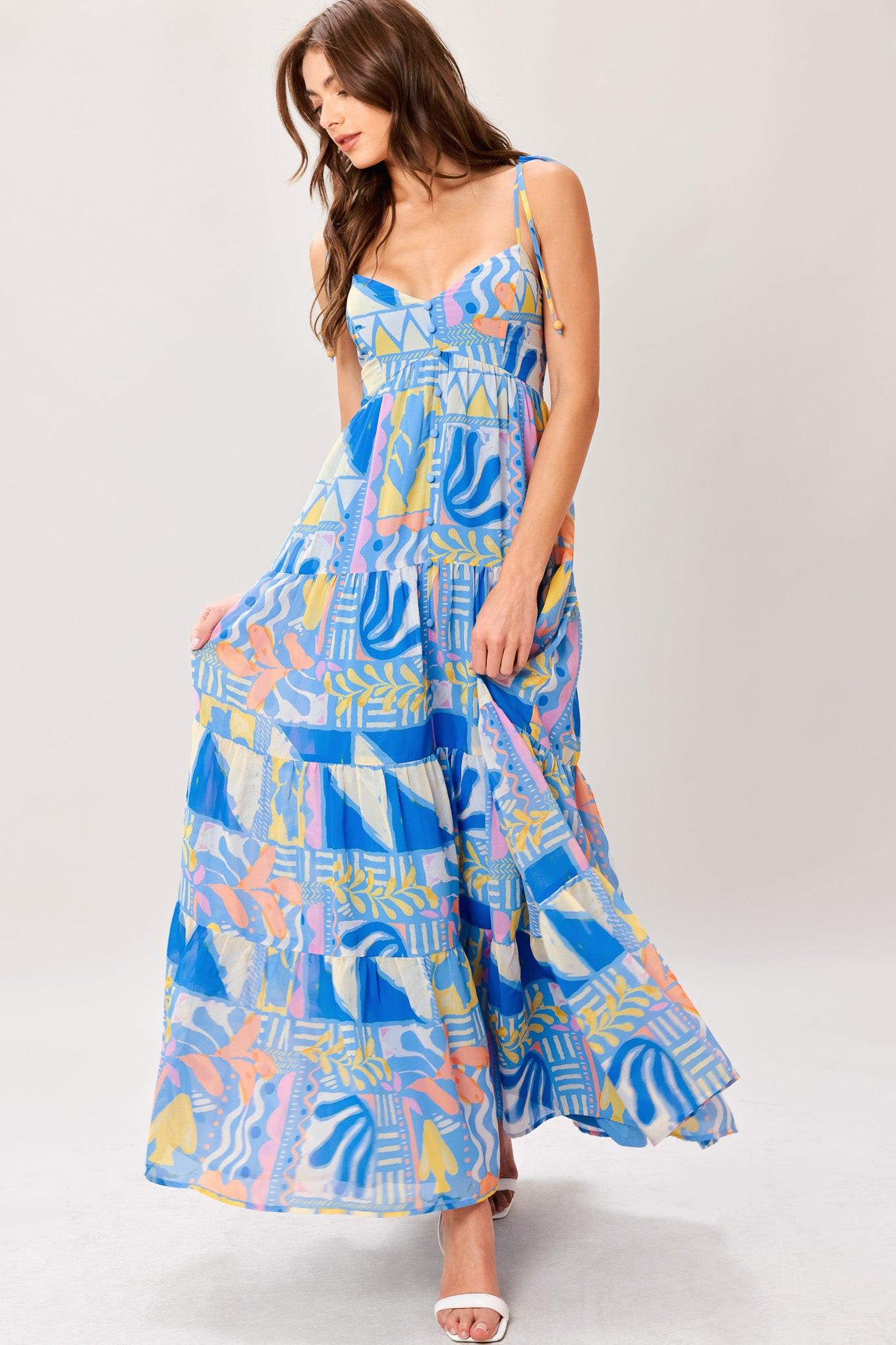 Woman wearing a colorful geometric patterned printed woven maxi dress featuring cami top with shoulder tie, front button detail, tier skirt and smocked back bodice
