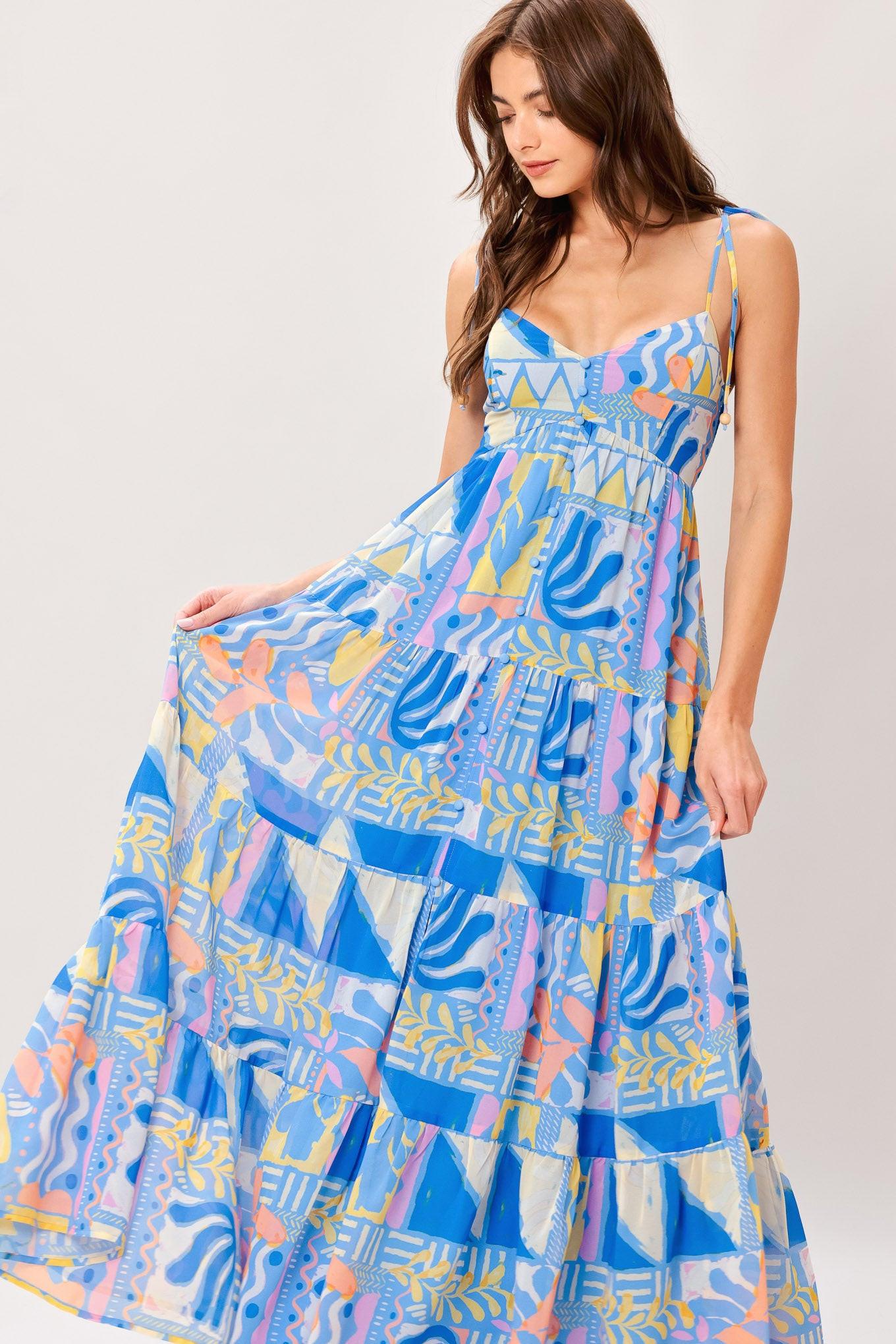 Woman wearing a colorful geometric patterned printed woven maxi dress featuring cami top with shoulder tie, front button detail, tier skirt and smocked back bodice
