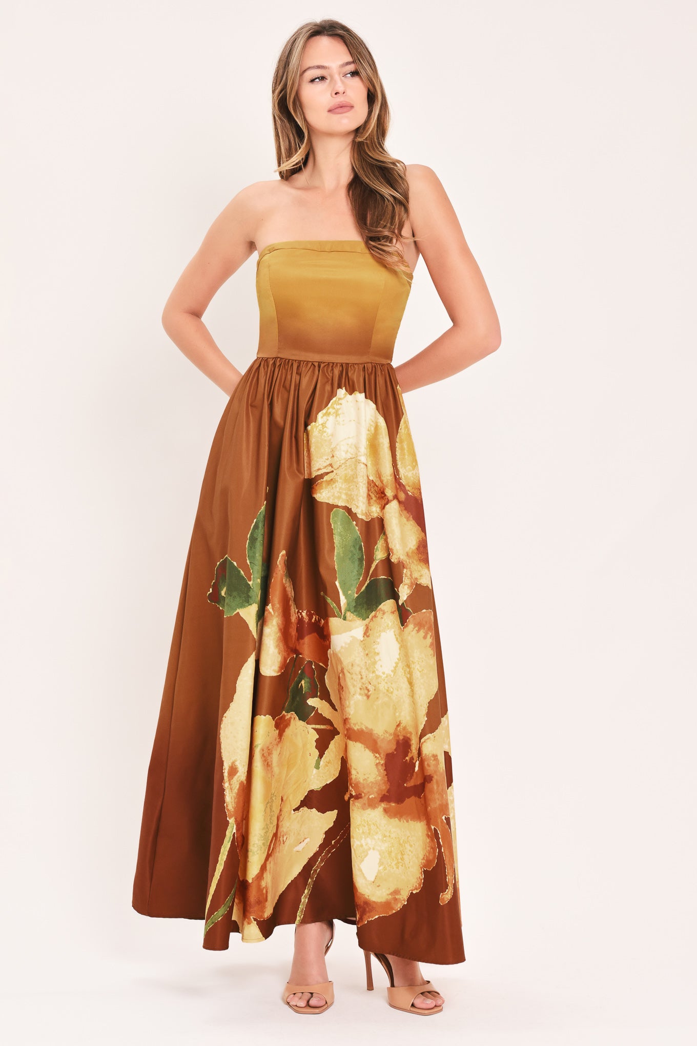 A woman modeling a strapless maxi dress with a mustard yellow bodice and a brown skirt featuring a large yellow floral print with green leaves | Flying Tomato